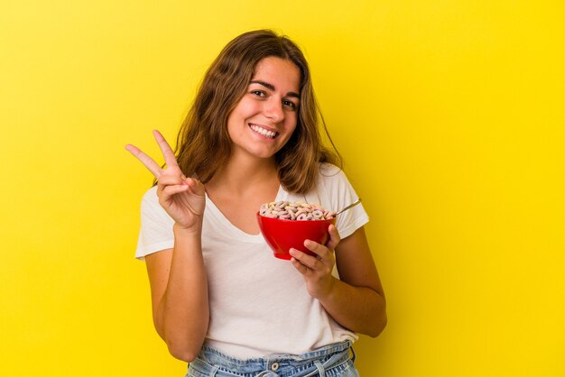 Young caucasian woman holding cereals isolated on yellow background  showing number two with fingers.