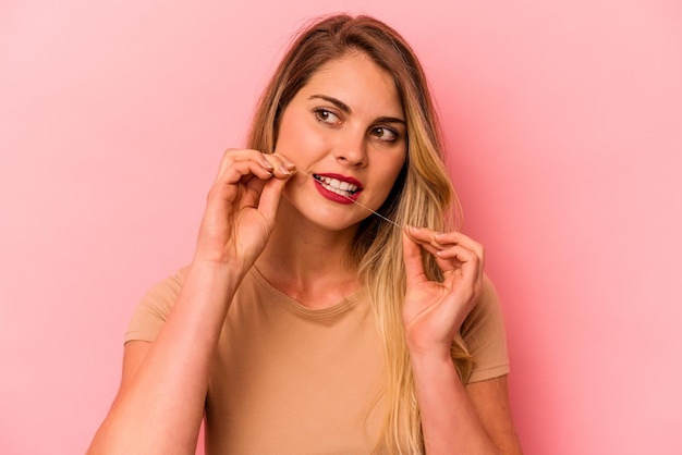 Young caucasian woman holding dental floss isolated on pink background