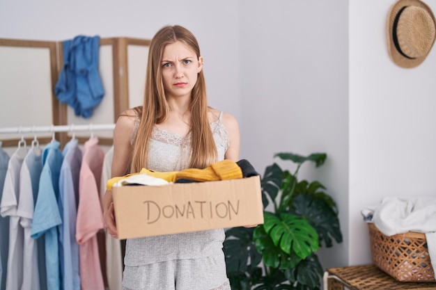 Young caucasian woman holding donations box for charity skeptic and nervous, frowning upset because of problem. negative person.