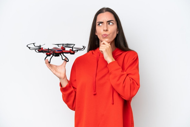 Young caucasian woman holding a drone isolated on white background having doubts and thinking