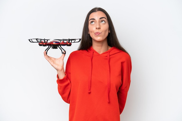 Young caucasian woman holding a drone isolated on white background and looking up