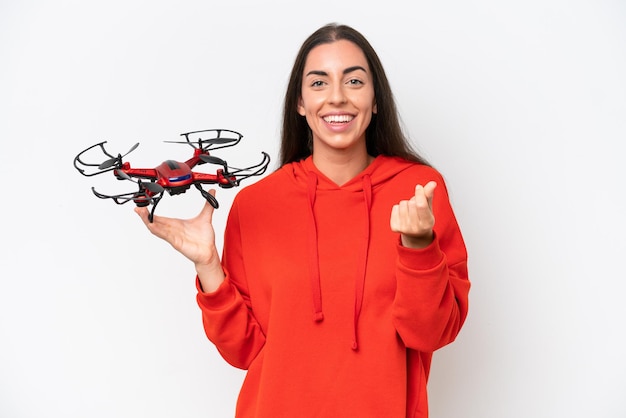 Young caucasian woman holding a drone isolated on white background making money gesture