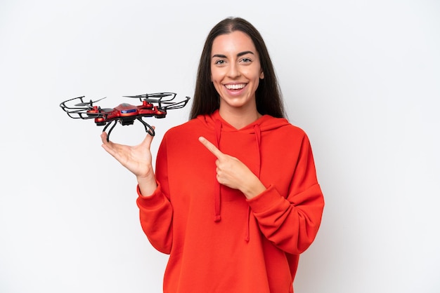 Young caucasian woman holding a drone isolated on white background pointing to the side to present a product