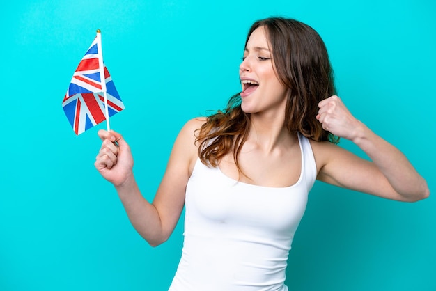 Young caucasian woman holding English flag isolated on blue background celebrating a victory