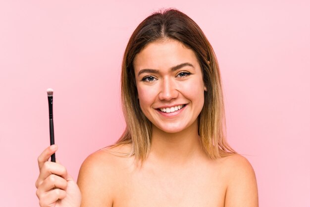 Young caucasian woman holding a eyebrush isolated happy, smiling and cheerful.