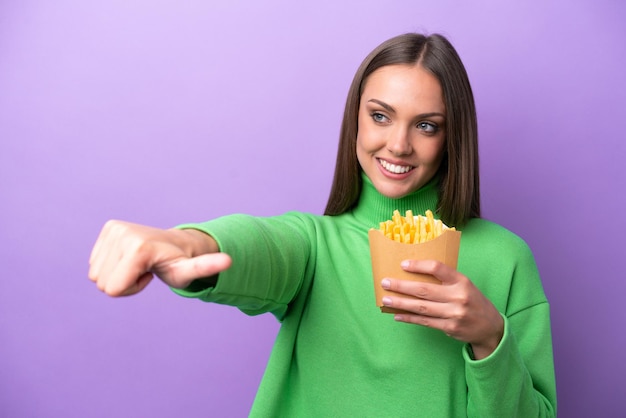 Young caucasian woman holding fried chips on purple background giving a thumbs up gesture