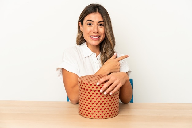 Young caucasian woman holding a gift box isolated smiling and pointing aside, showing something at blank space.