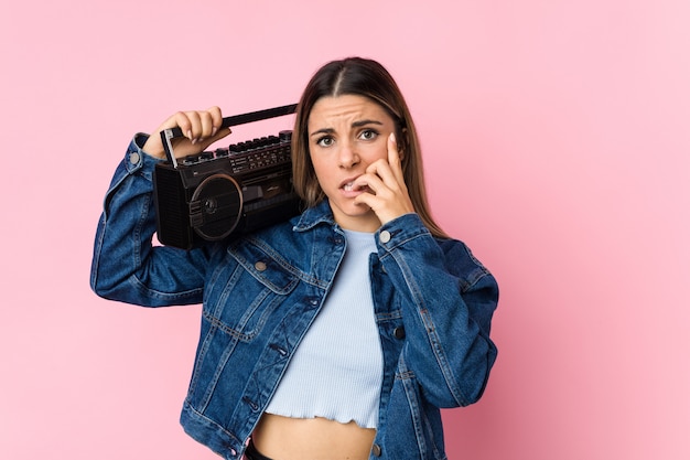 Young caucasian woman holding a guetto blaster biting fingernails, nervous and very anxious.