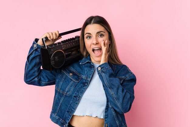 Young caucasian woman holding a guetto blaster shouting excited to front.