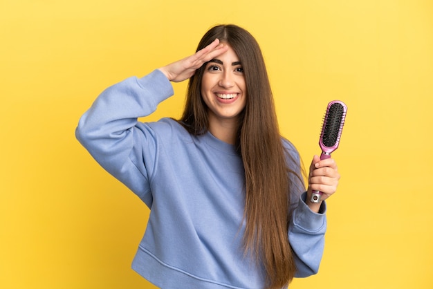 Photo young caucasian woman holding hairbrush isolated on blue background with surprise expression