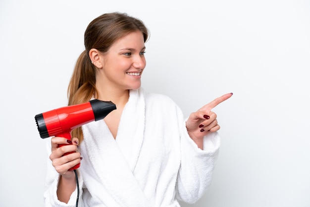 Young caucasian woman holding hairdryer isolated on white background pointing to the side to present a product