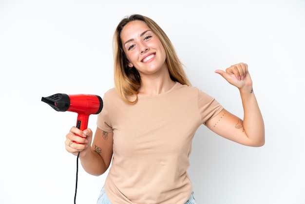 Young caucasian woman holding a hairdryer isolated on white background proud and selfsatisfied