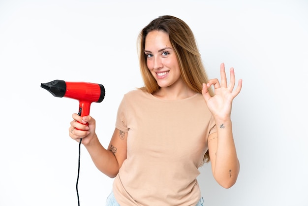 Young caucasian woman holding a hairdryer isolated on white background showing ok sign with fingers