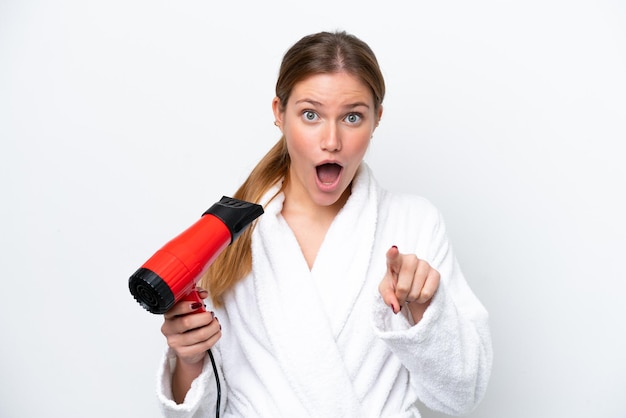 Young caucasian woman holding hairdryer isolated on white background surprised and pointing front