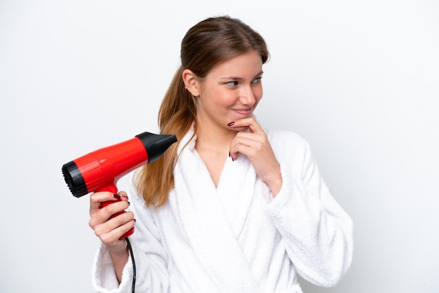 Young caucasian woman holding hairdryer isolated on white background thinking an idea and looking side