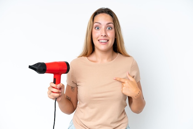 Young caucasian woman holding a hairdryer isolated on white background with surprise facial expression