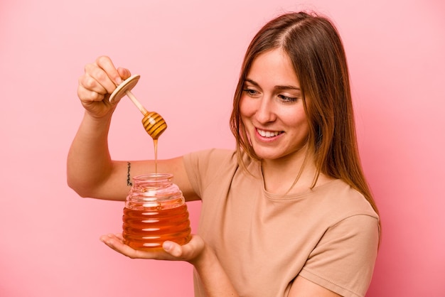 Young caucasian woman holding honey isolated on pink background