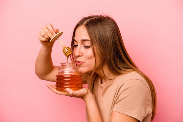 Young caucasian woman holding honey isolated on pink background