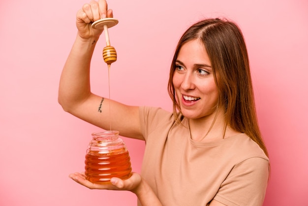 Young caucasian woman holding honey isolated on pink background