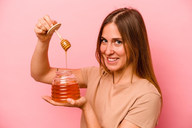 Young caucasian woman holding honey isolated on pink background