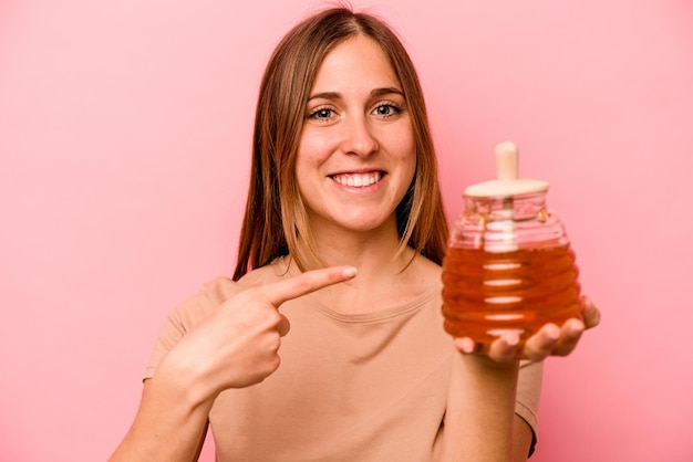 Young caucasian woman holding honey isolated on pink background