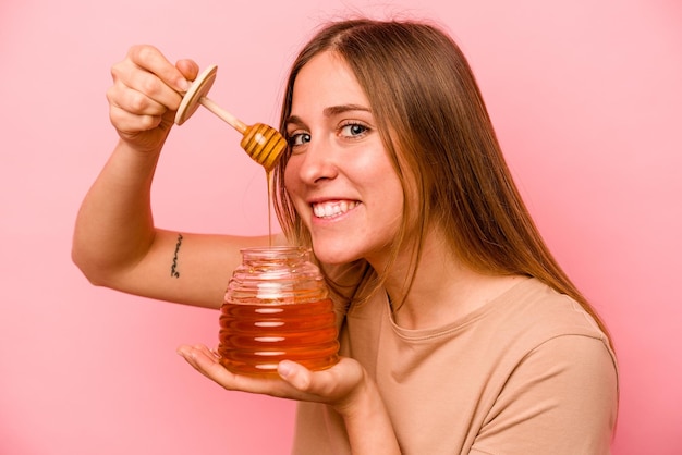 Young caucasian woman holding honey isolated on pink background