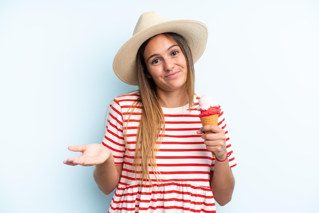 Young caucasian woman holding an ice cream isolated on blue background making doubts gesture while lifting the shoulders