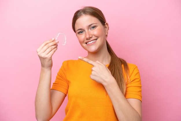 Young caucasian woman holding invisaging isolated on pink background and pointing it