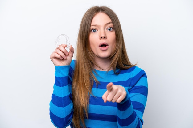 Young caucasian woman holding invisible braces isolated on white background surprised and pointing front