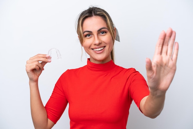 Young caucasian woman holding invisible braces on white background saluting with hand with happy expression