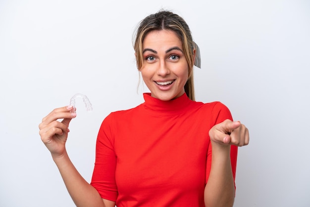 Young caucasian woman holding invisible braces on white background surprised and pointing front