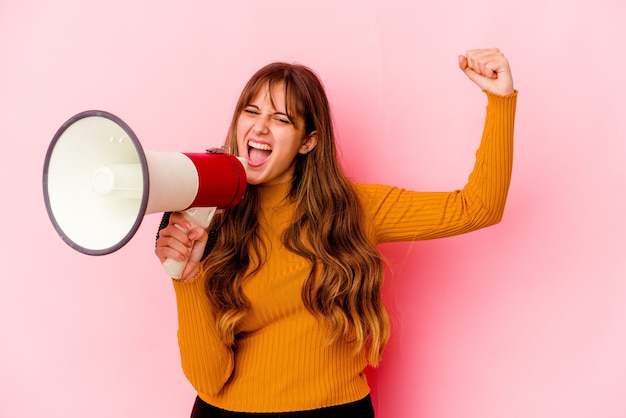 Photo young caucasian woman holding a megaphone isolated raising fist after a victory, winner concept.