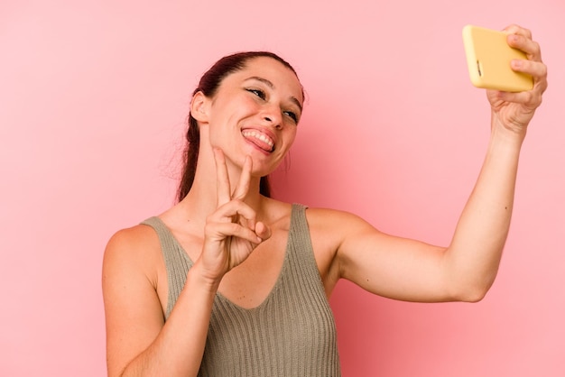 Young caucasian woman holding mobile phone isolated on pink background