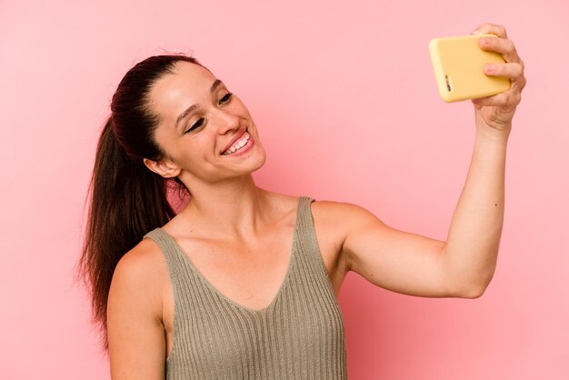 Young caucasian woman holding mobile phone isolated on pink background