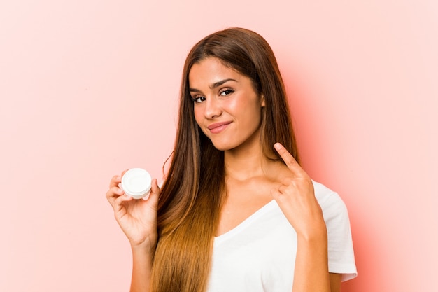 Young caucasian woman holding a moisturizer pointing with finger at you