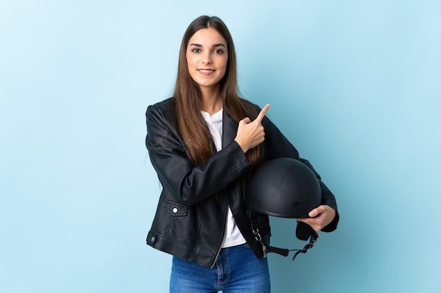 Young caucasian woman holding a motorcycle helmet on blue pointing to the side to present a product