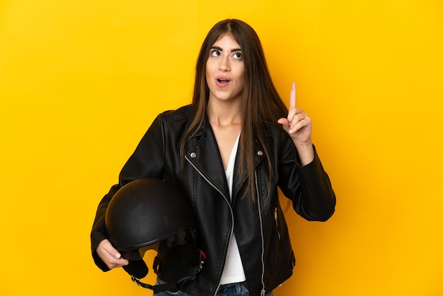 Young caucasian woman holding a motorcycle helmet isolated on yellow background intending to realizes the solution while lifting a finger up