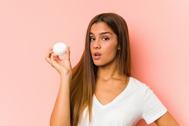 Young caucasian woman holding a mousturizer isolated on a pink wall