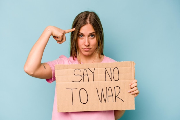 Young caucasian woman holding no war placard isolated on blue background