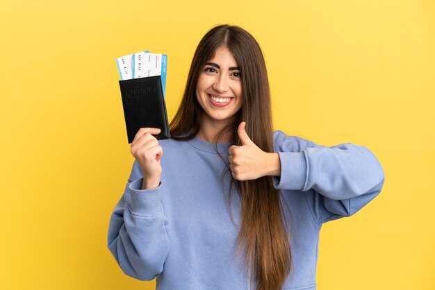 Young caucasian woman holding a passport isolated on yellow background giving a thumbs up gesture