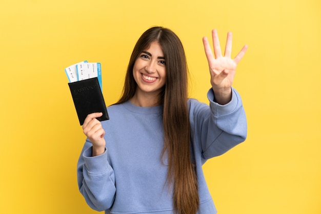 Young caucasian woman holding a passport isolated on yellow background happy and counting four with fingers