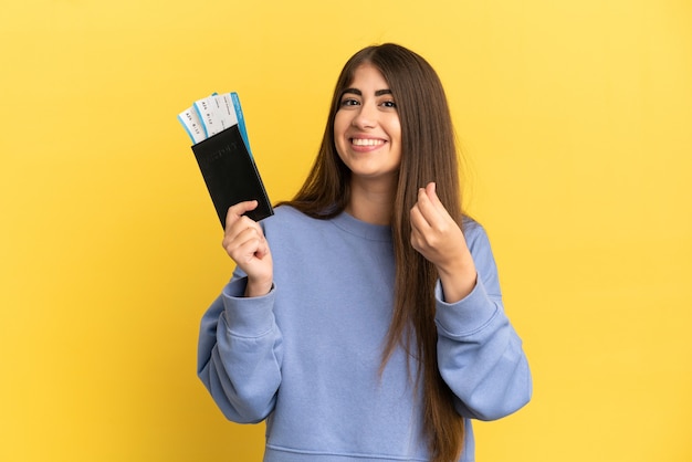 Young caucasian woman holding a passport isolated on yellow background making money gesture