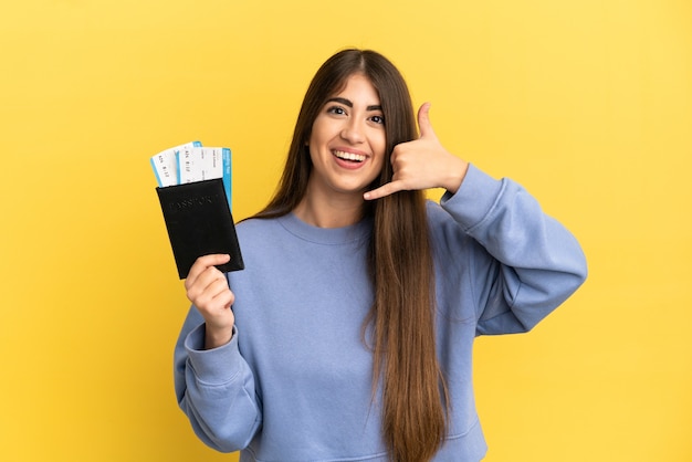 Young caucasian woman holding a passport isolated on yellow background making phone gesture. Call me back sign