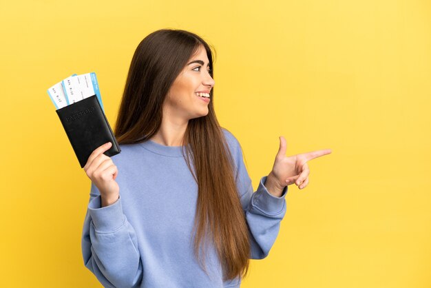 Young caucasian woman holding a passport isolated on yellow background pointing finger to the side