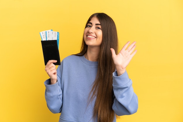 Young caucasian woman holding a passport isolated on yellow background saluting with hand with happy expression