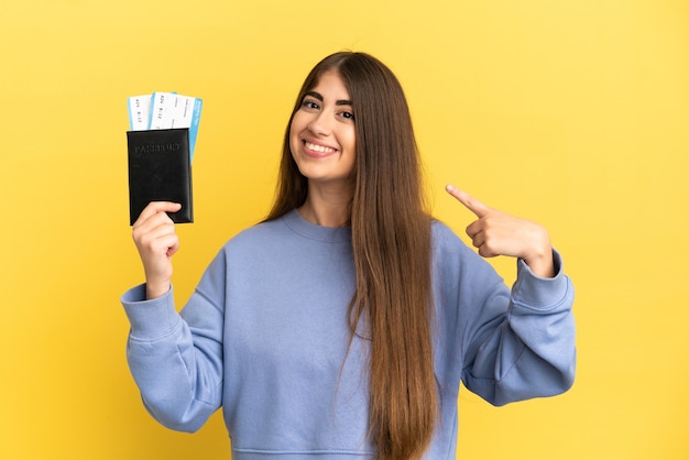 Young caucasian woman holding a passport isolated on yellow wall giving a thumbs up gesture