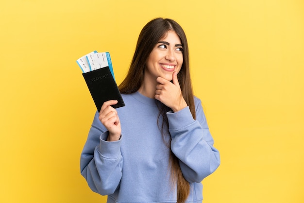 Young caucasian woman holding a passport isolated on yellow wall looking to the side and smiling