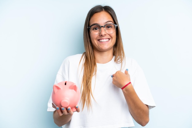 Young caucasian woman holding a piggybank isolated on blue background with surprise facial expression