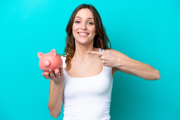 Young Caucasian woman holding a piggybank isolated on blue bakcground with surprise facial expression