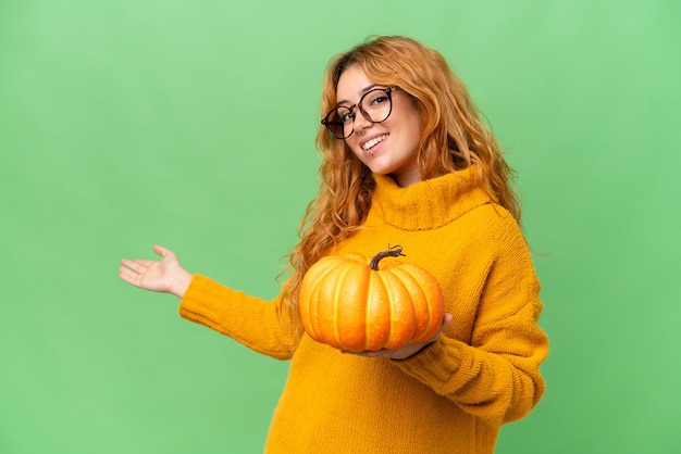 Young caucasian woman holding a pumpkin isolated on green screen chroma key background extending hands to the side for inviting to come